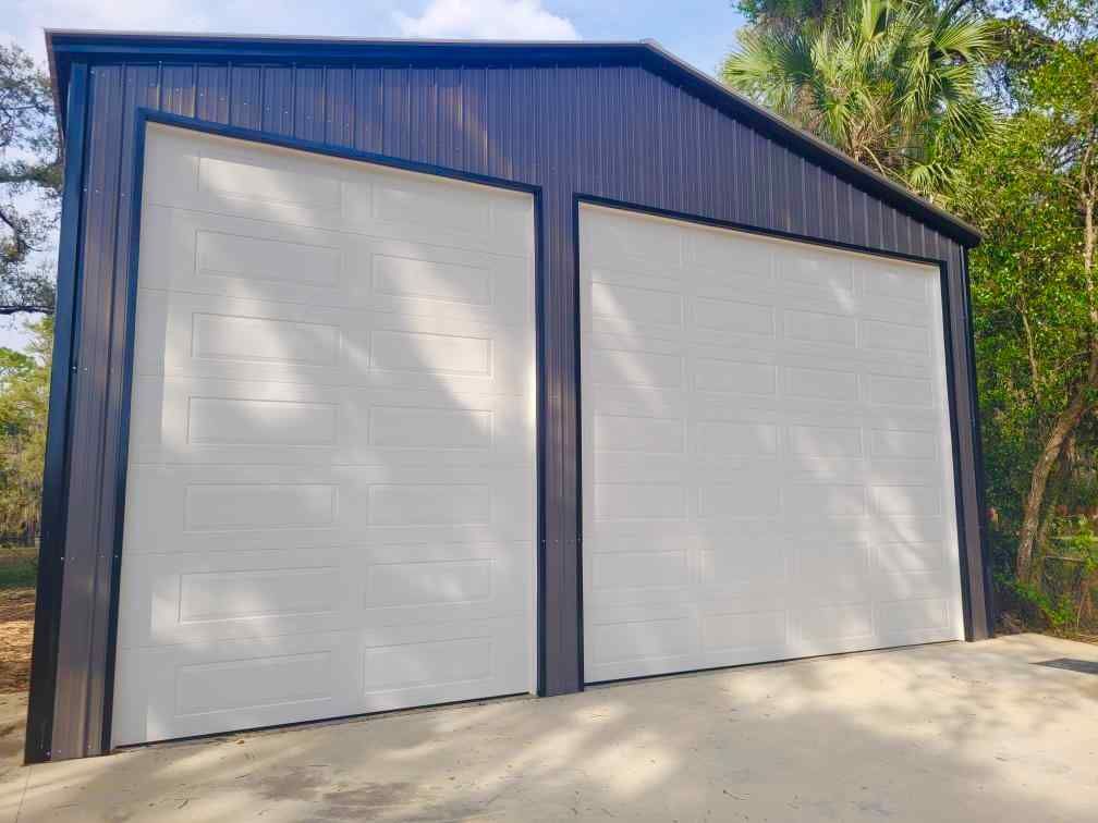 A dark-trimmed metal building with two new white garage doors